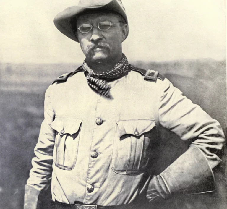 Photograph of Theodore Roosevelt standing confidently in a military uniform. Roosevelt's strong presence is evident as he stands tall, his uniform. His focused gaze and firm stance reflect his leadership and commitment. The uniform's details and Roosevelt's demeanor evoke a sense of authority and determination, encapsulating his role as a historic figure and military leader.