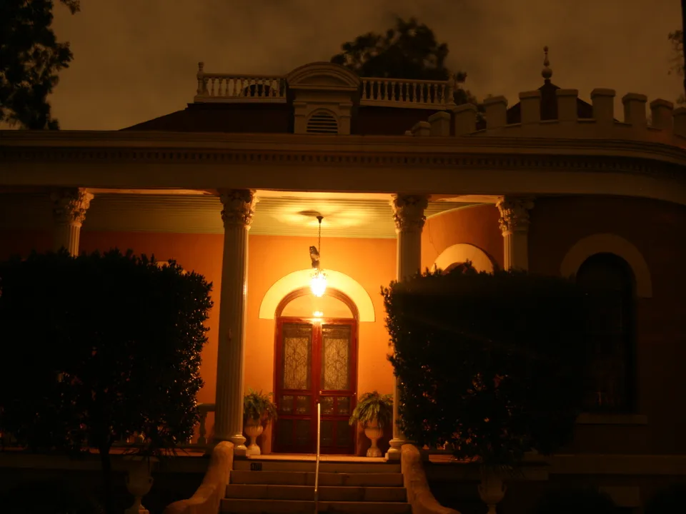 A nighttime view of the reputedly haunted house of Miss Margret, part of the Alamo Street Theater, featuring the house's illuminated entrance with a classic architectural style.
